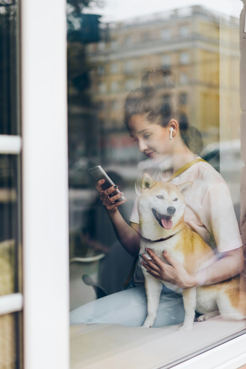 a woman sitting on a window sill holding a dog