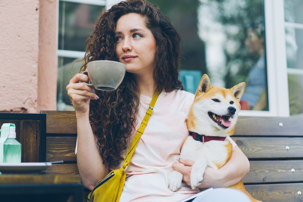 a woman sitting on a bench holding a cup and a dog