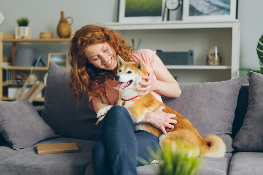 eine Frau, die auf einer Couch sitzt und einen Hund hält