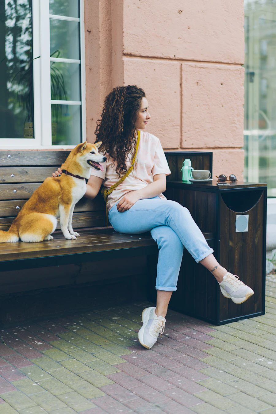 A student sitting on a bench outside a building with her dog beside her