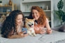 two women laying on a bed with a dog
