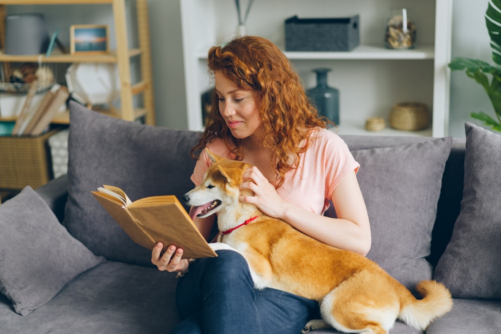 uma mulher sentada em um sofá com um cachorro lendo um livro