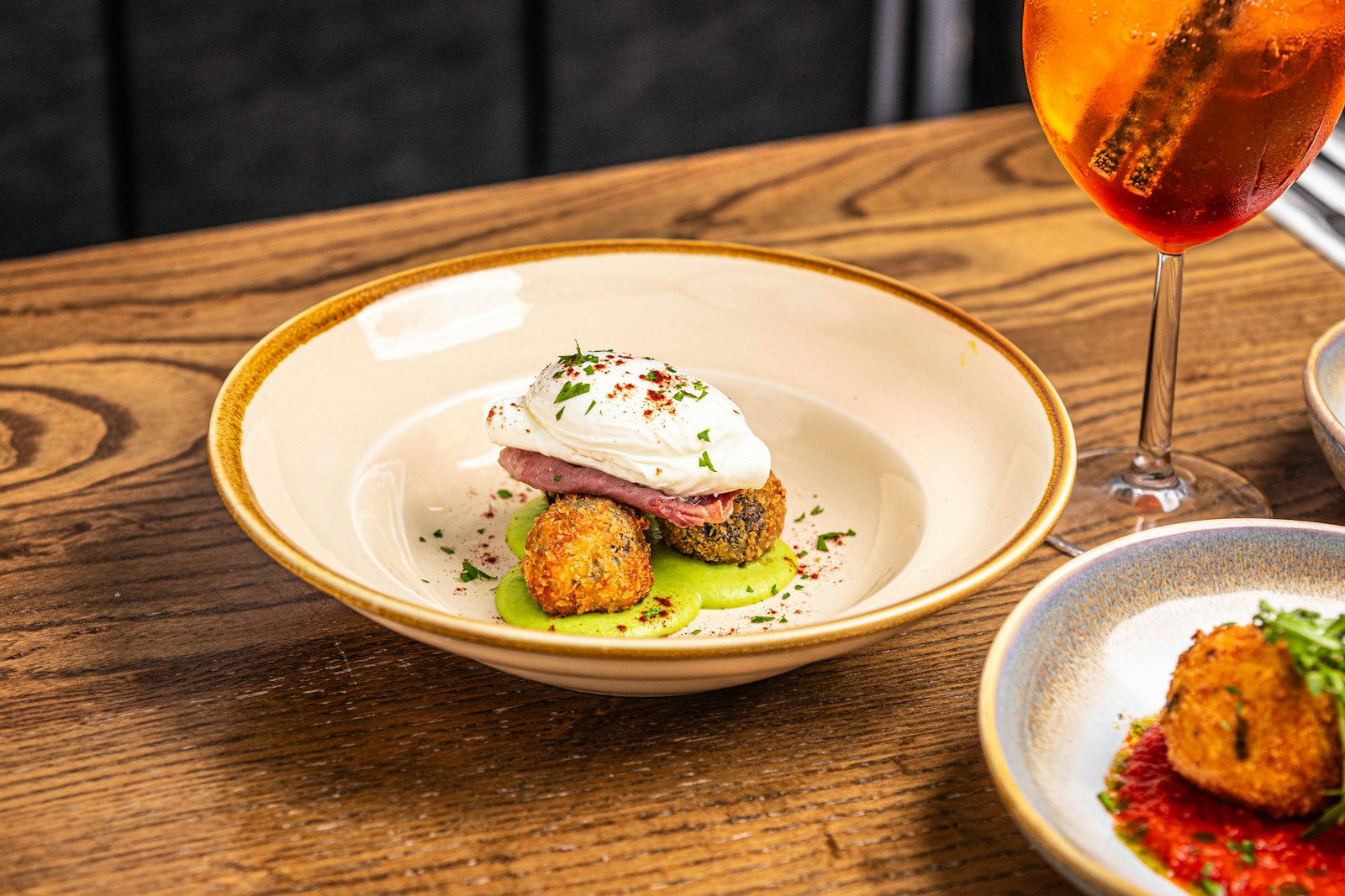 Une assiette creuse avec une burrata, deux croquettes dorées et une huile verte