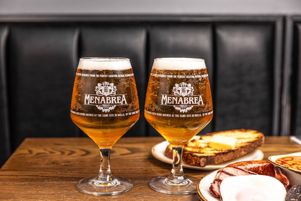 two glasses of beer sitting on top of a wooden table