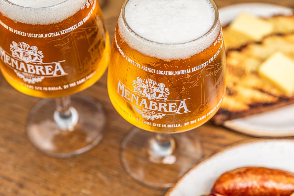 two glasses of beer and a plate of food on a table