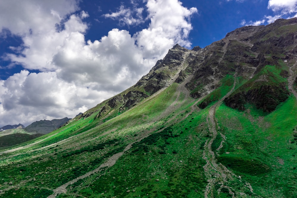 a view of a green mountain with clouds in the sky