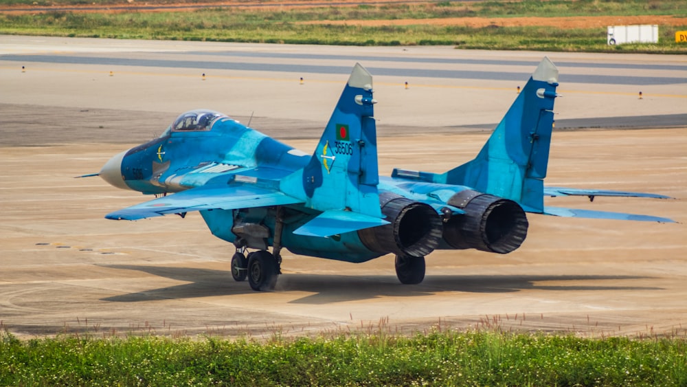 a blue fighter jet sitting on top of an airport tarmac