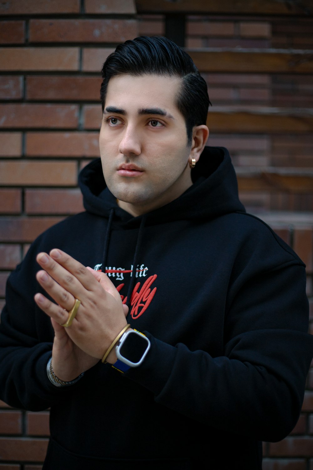 a man in a black hoodie standing in front of a brick wall
