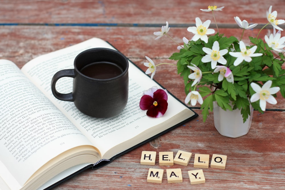 a cup of coffee next to a book and flowers