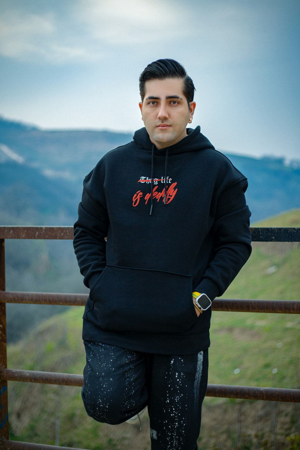 a man standing in front of a fence wearing a black hoodie