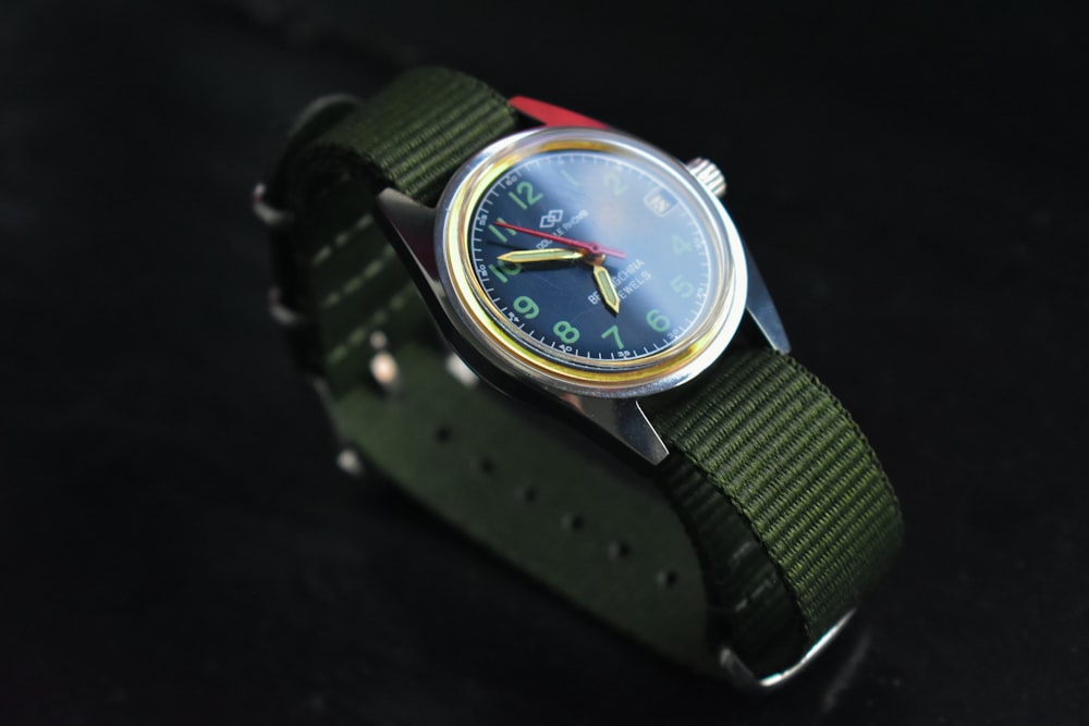 a watch with a green strap on a black surface