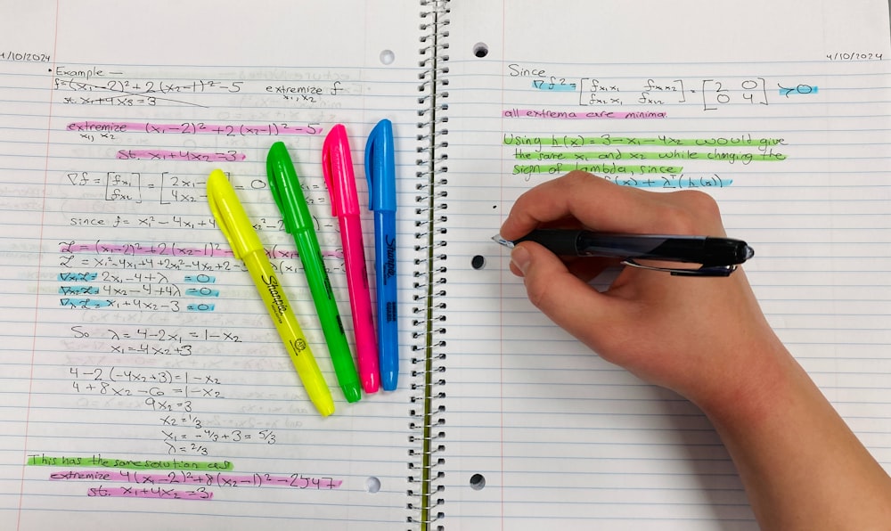 a person writing on a notebook with colored pens