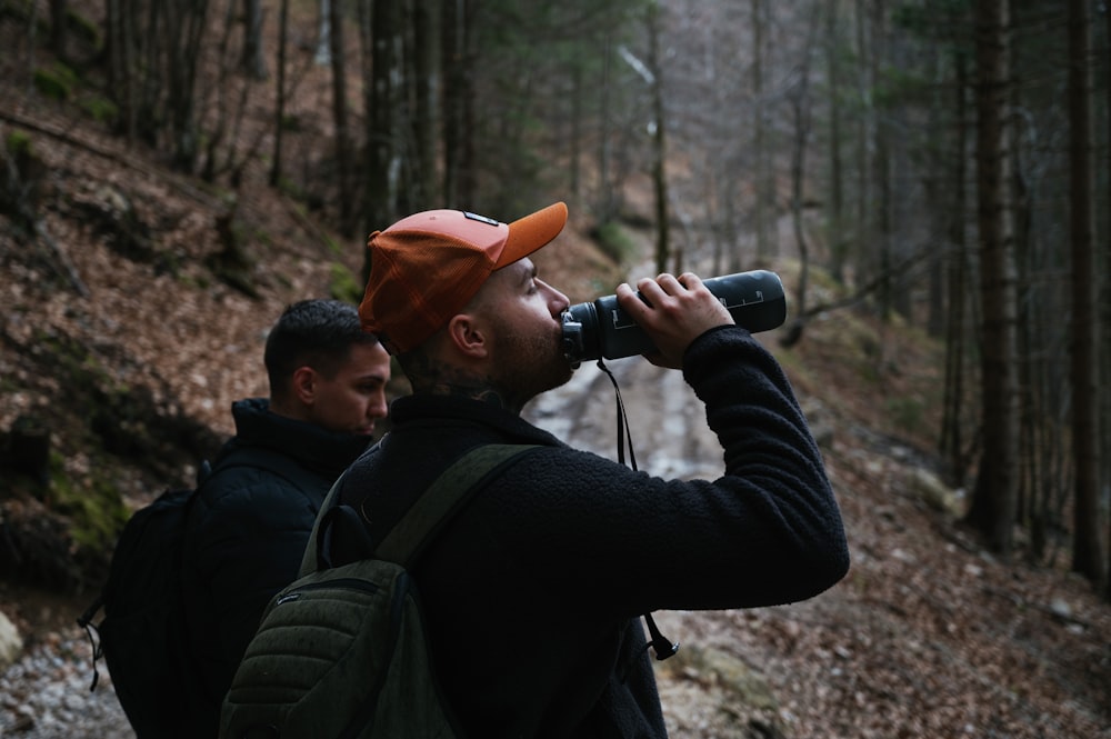 a man wearing a hat and carrying a backpack is looking through a pair of binoculars