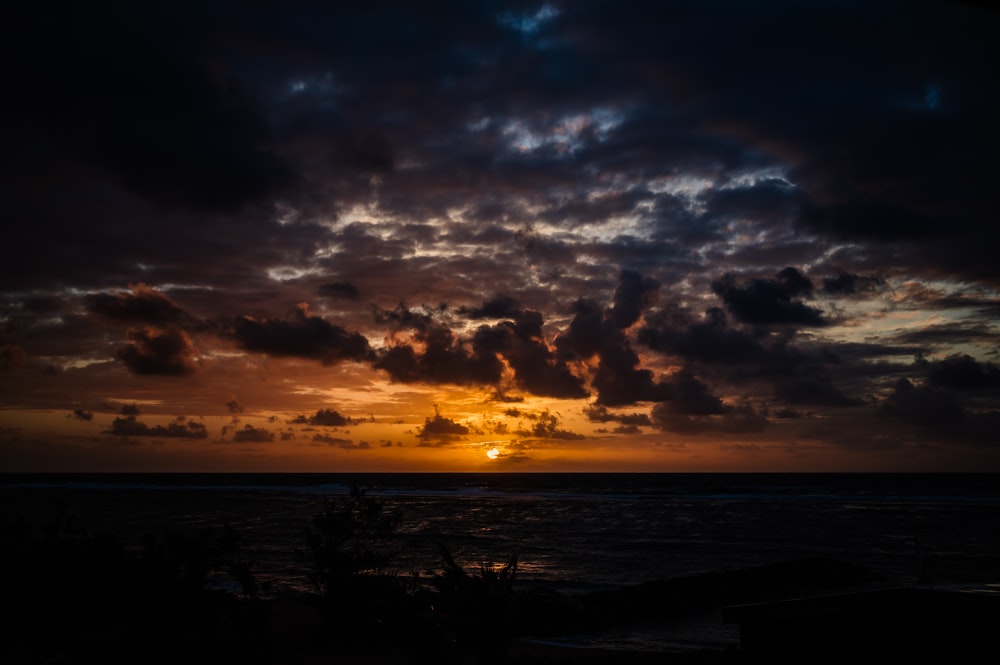 the sun is setting over the ocean with clouds