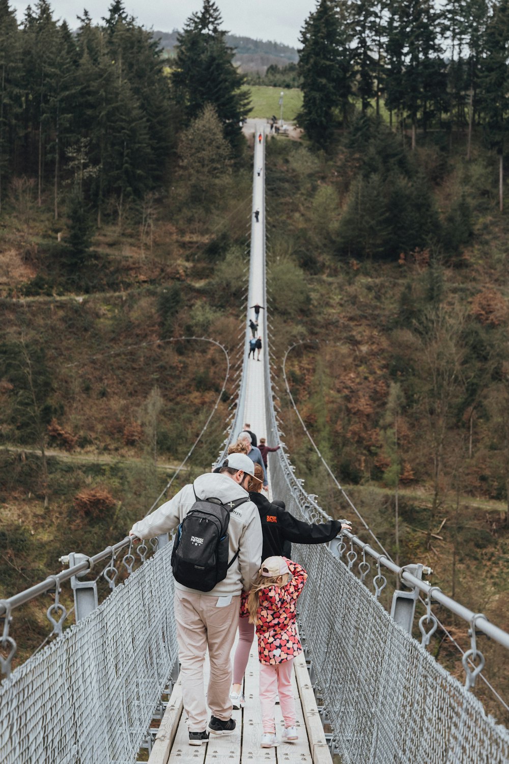 a man and a little girl walking across a suspension bridge