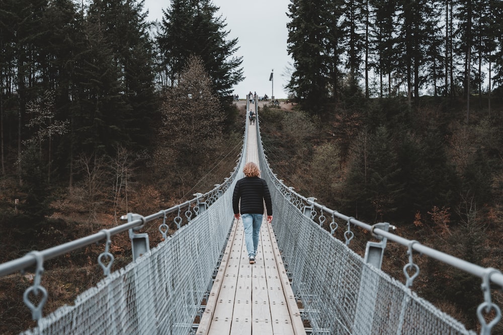 a man walking across a suspension bridge in the woods