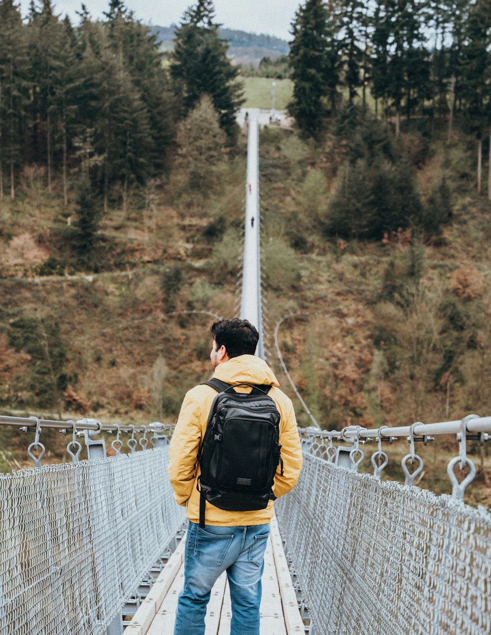 a man walking across a suspension bridge in the woods