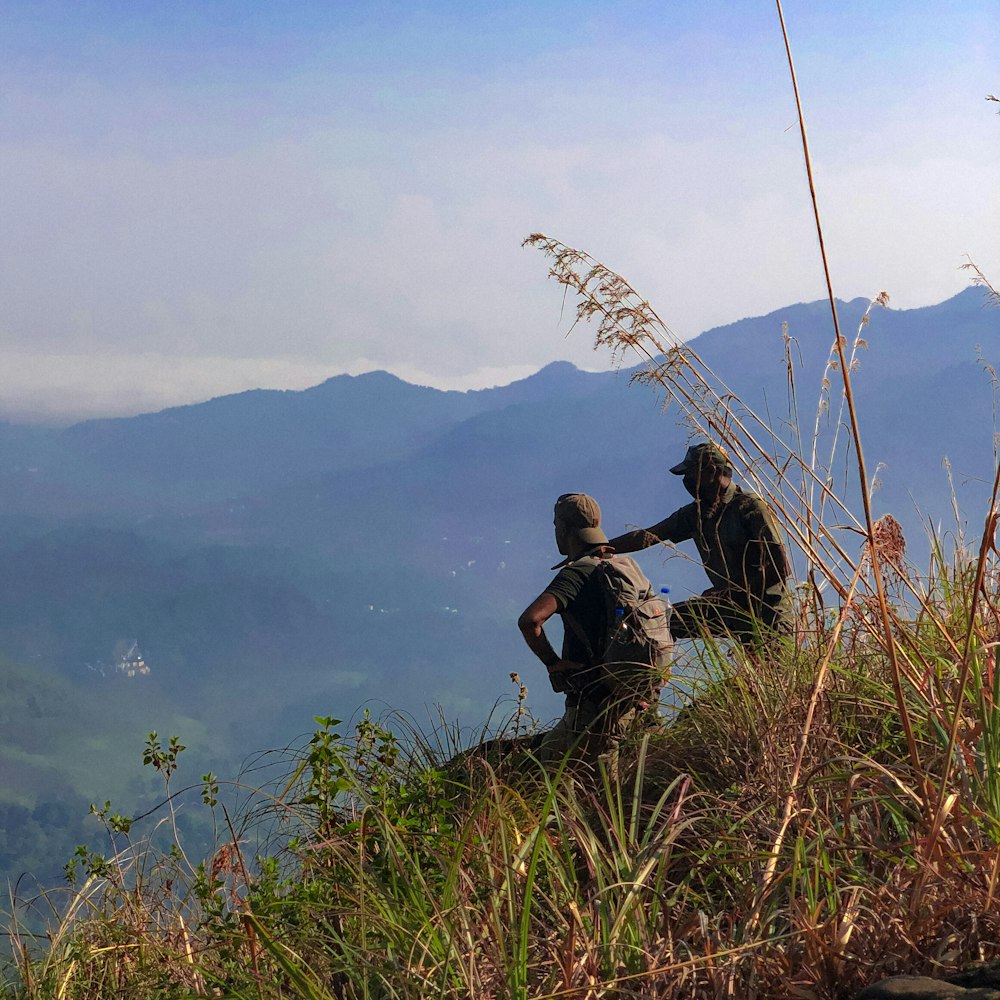 two people sitting on top of a hill with mountains in the background