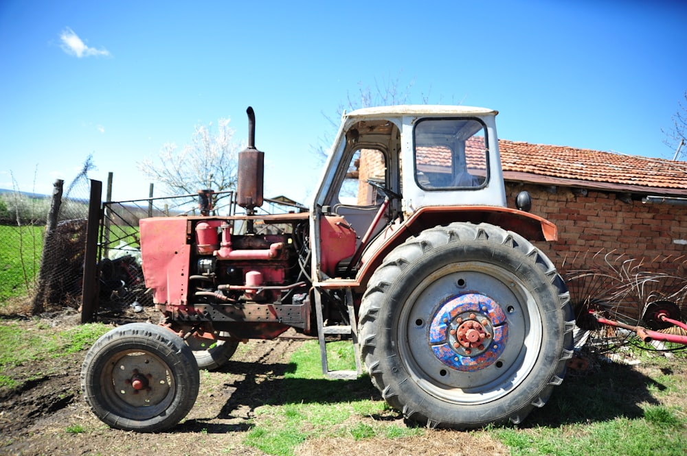 a red tractor parked in a field next to a brick building