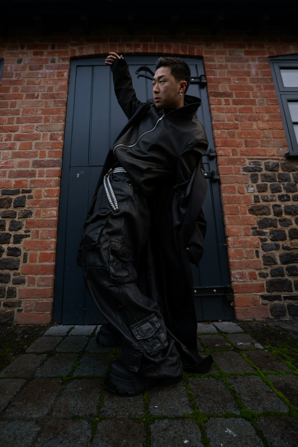 a man in a black outfit standing in front of a brick building