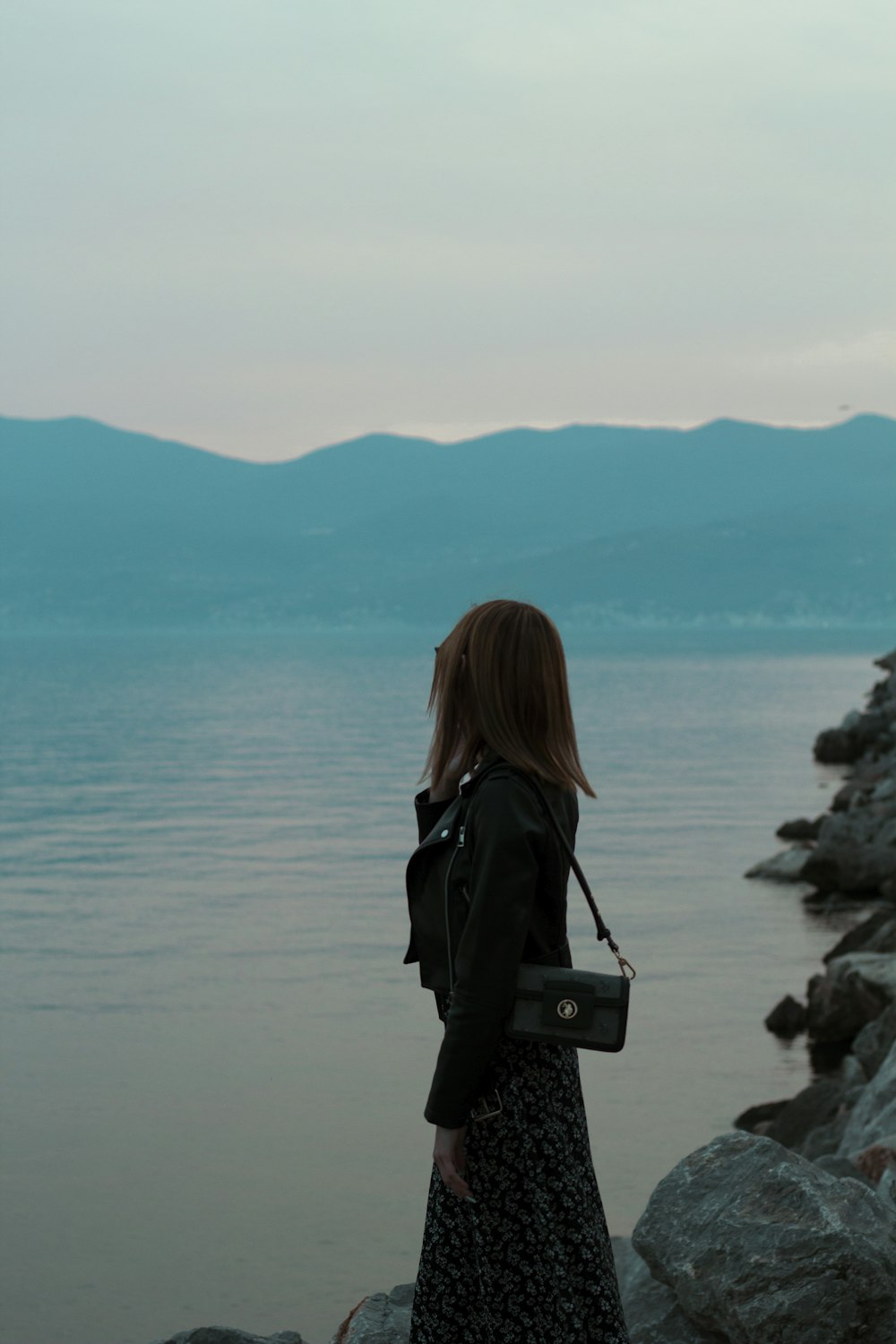 a woman standing on a rocky shore next to a body of water