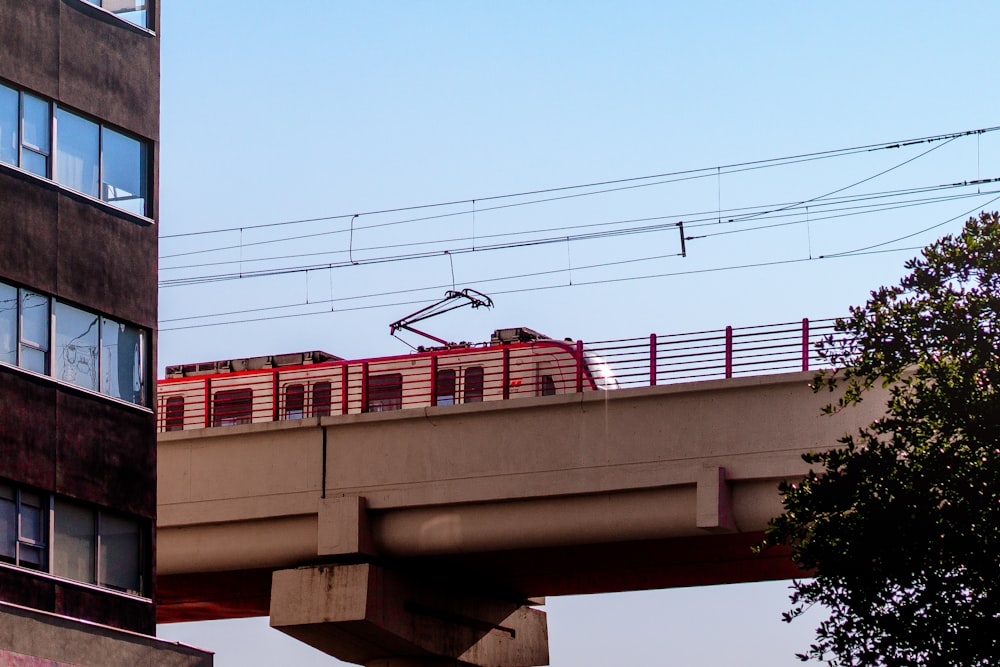 a red train traveling over a bridge next to a tall building