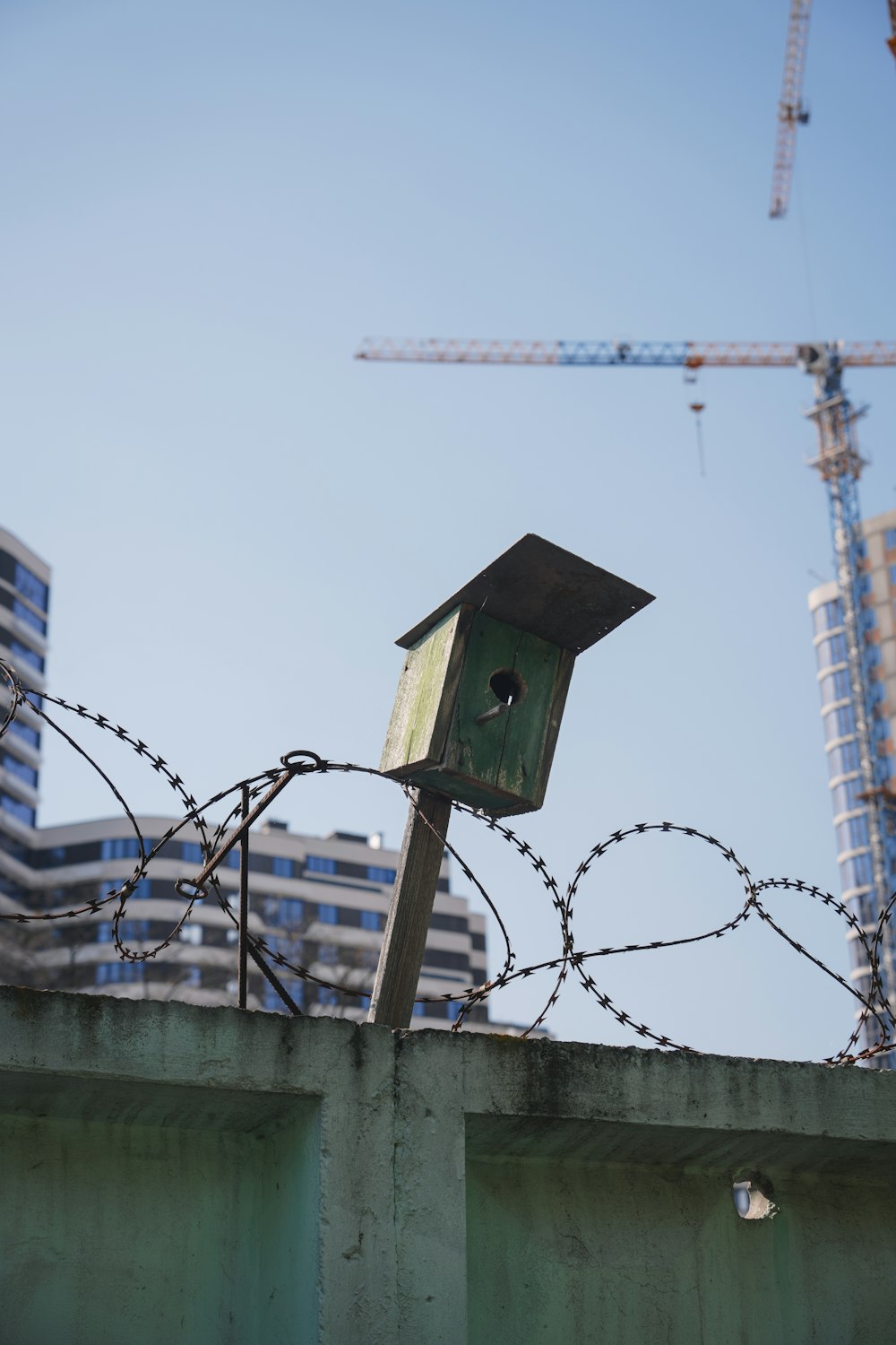 a birdhouse on top of a fence with a building in the background