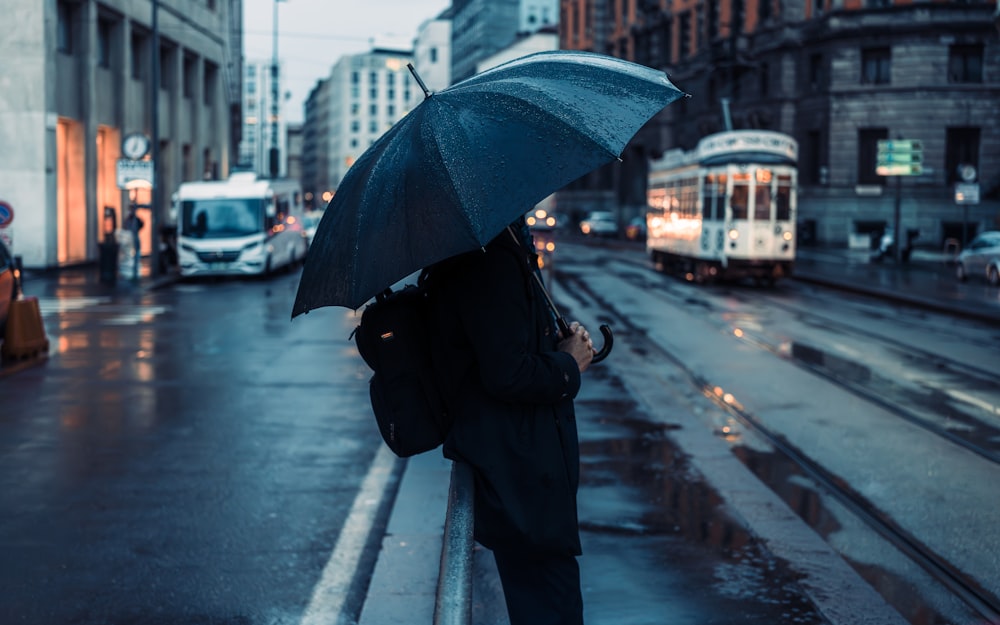 eine Person, die auf einer Straße steht und einen Regenschirm hält