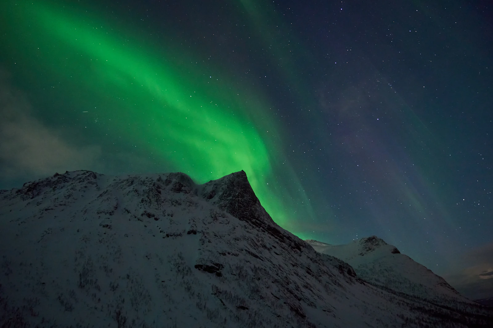 Green and purple aurora above a snow-covered mountain at the Bergsbotn viewpoint on Senja
