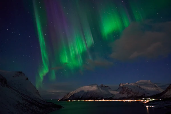 Green and purple aurora reflected in still water below the mountains at Bergsbotn on Senja