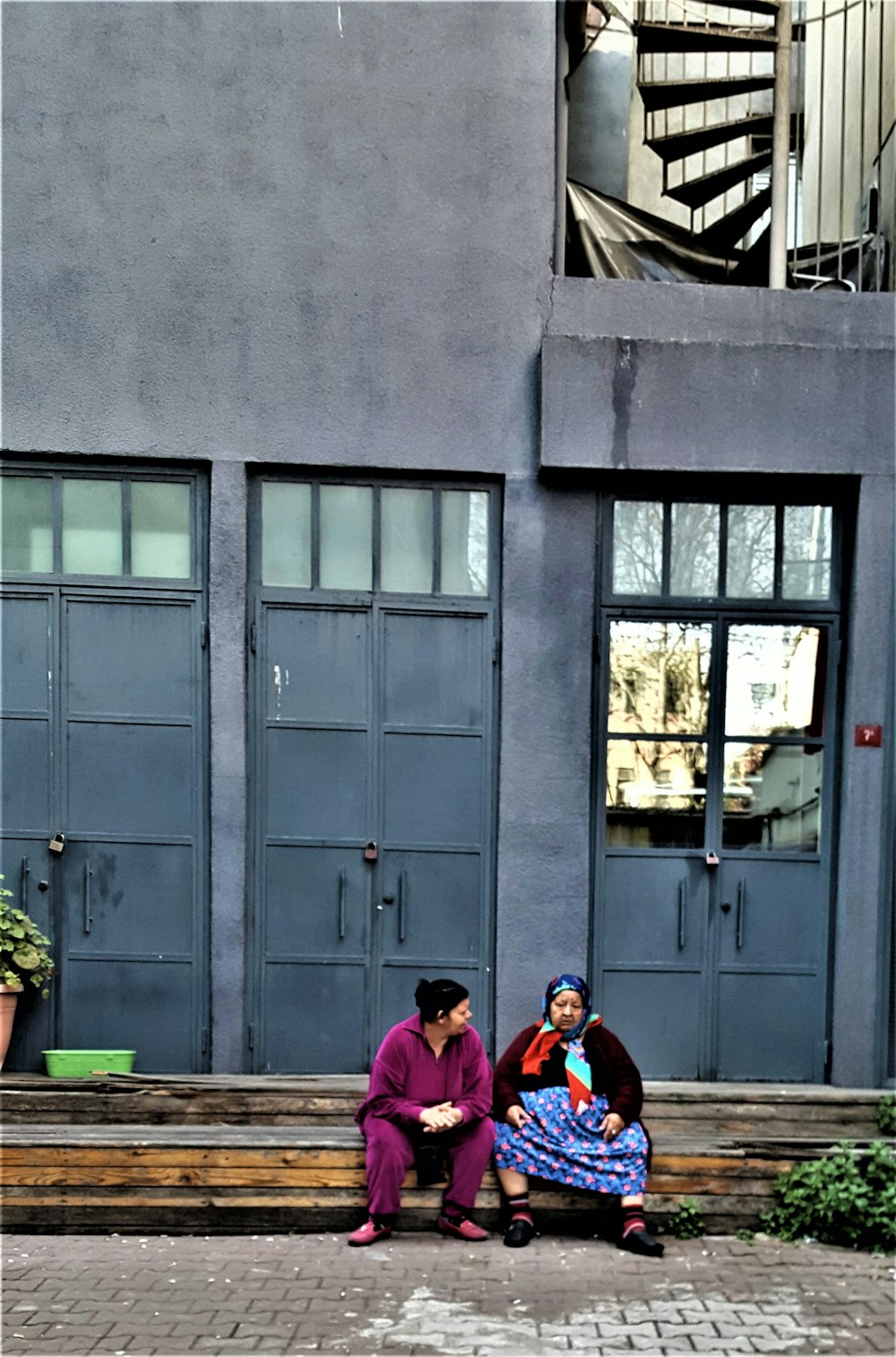 two women sitting on a bench in front of a building