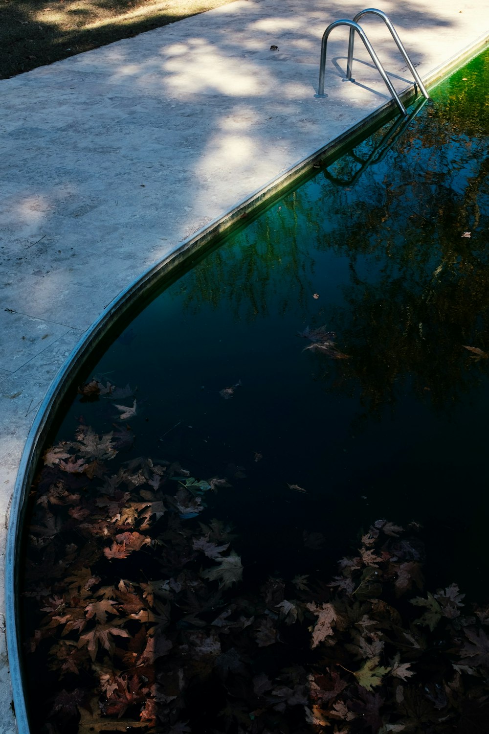 an empty swimming pool with leaves on the ground
