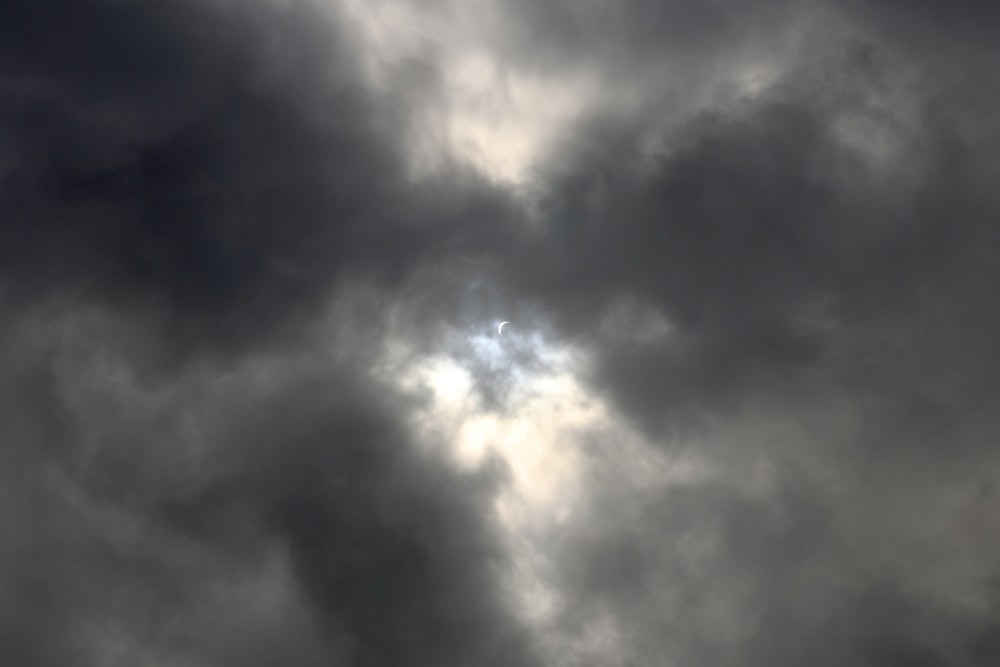 a plane flying through a cloudy sky with the sun peeking through the clouds
