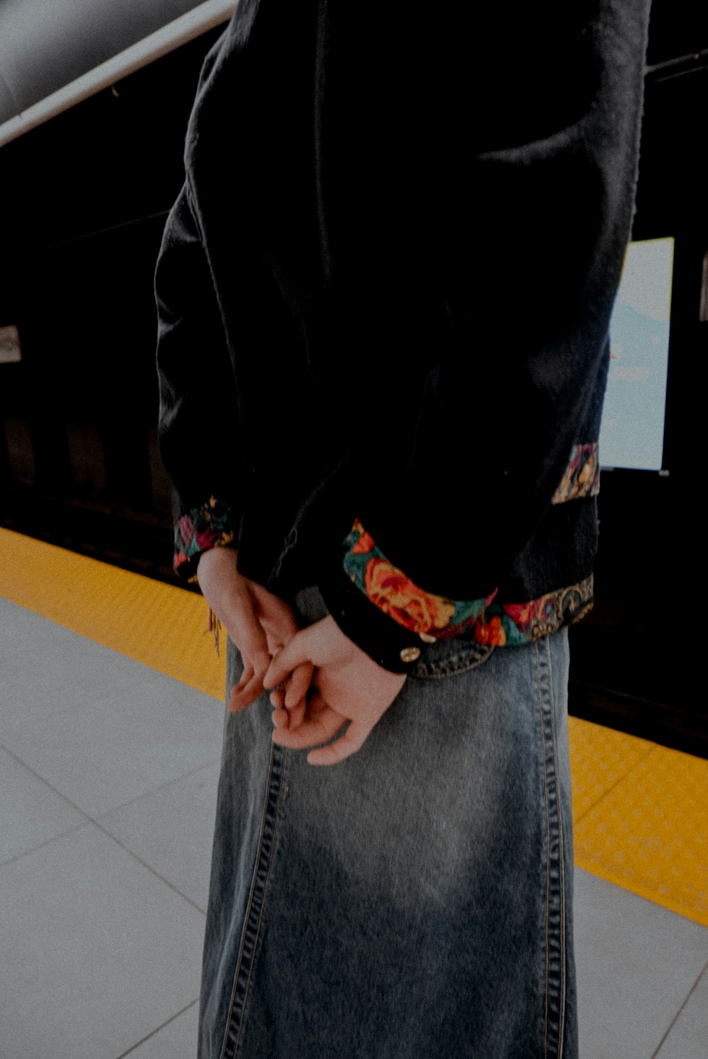 a person standing on a subway platform with their hands in their pockets