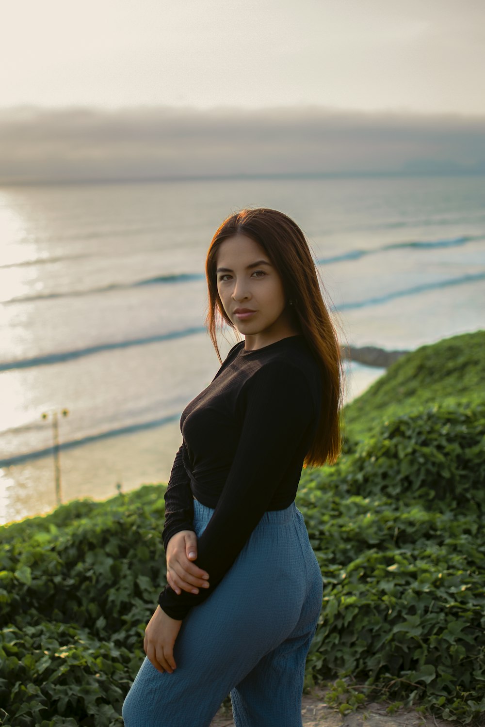 a woman standing on top of a hill next to the ocean