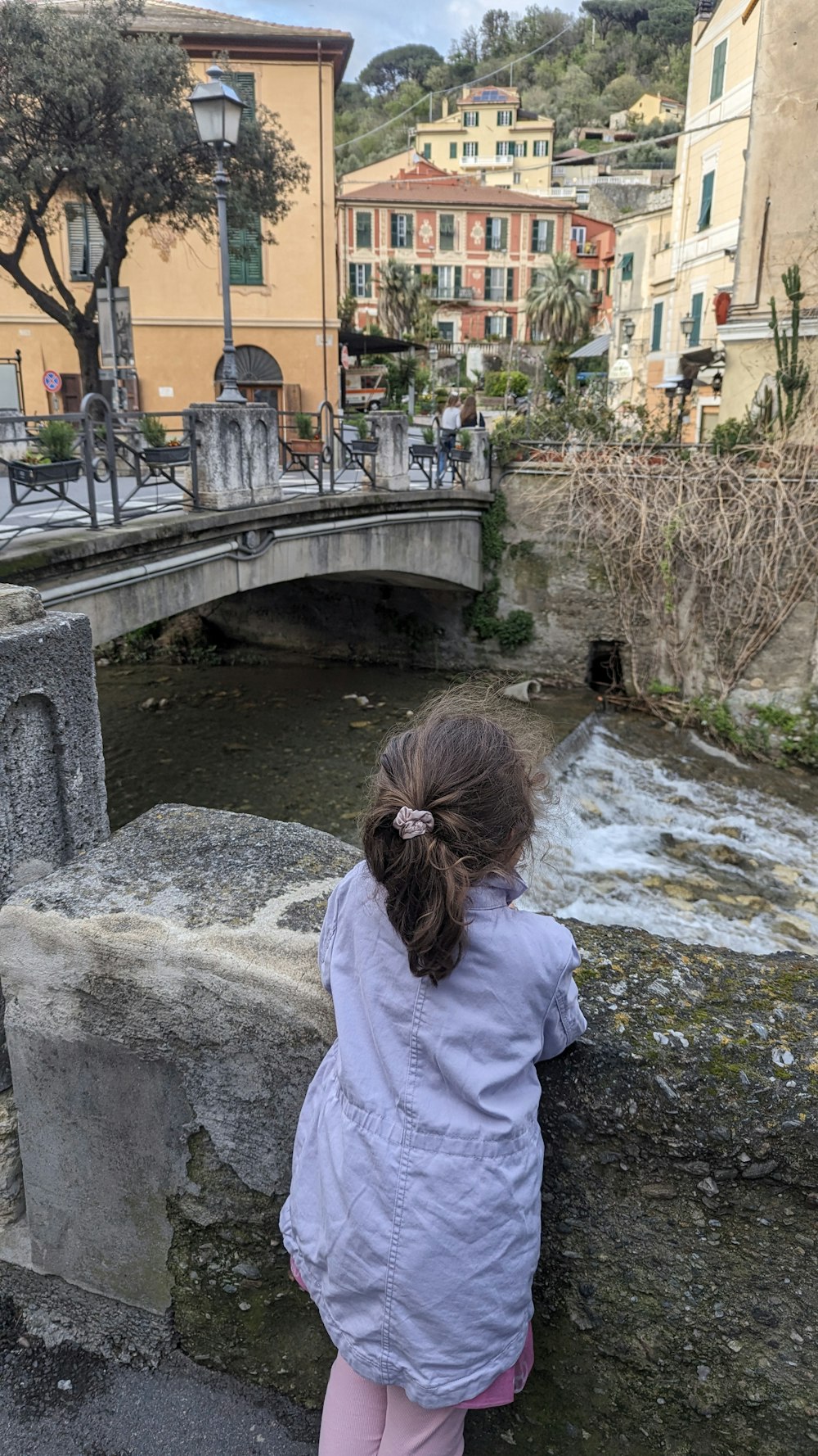 uma menina em pé em uma ponte olhando para a água
