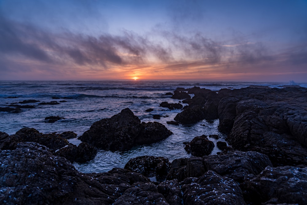 the sun is setting over the ocean and rocks