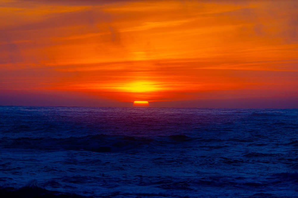 the sun is setting over the ocean on a cloudy day