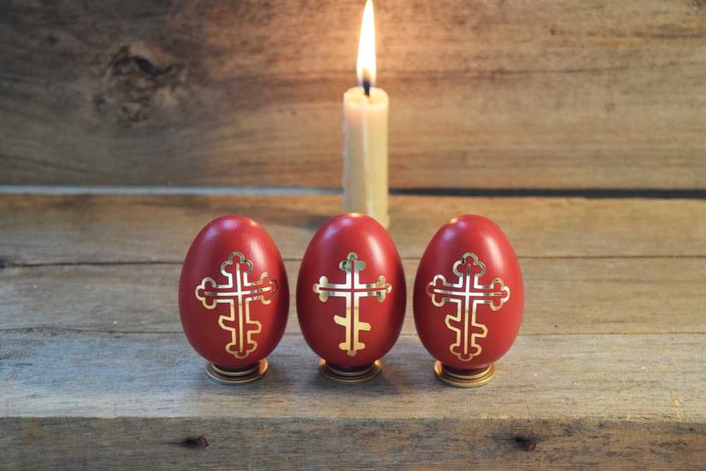 three red eggs with a cross painted on them next to a lit candle