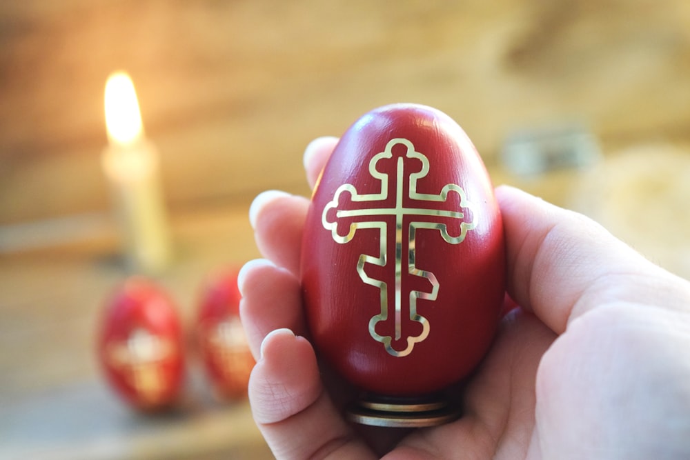 a hand holding an egg with a cross painted on it