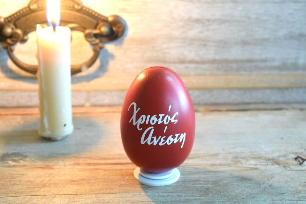 a red egg sitting on top of a table next to a candle