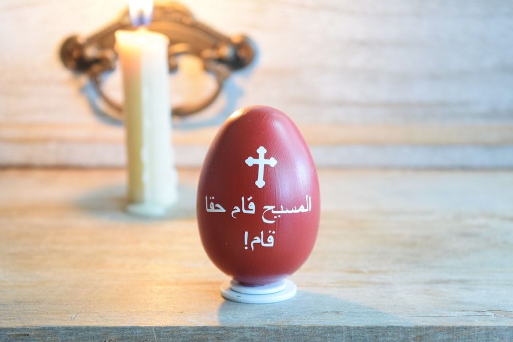 a red egg sitting on top of a table next to a candle