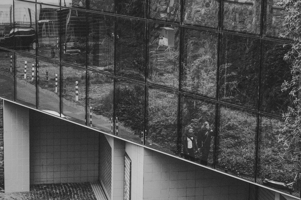 a black and white photo of a building with a reflection of people in it