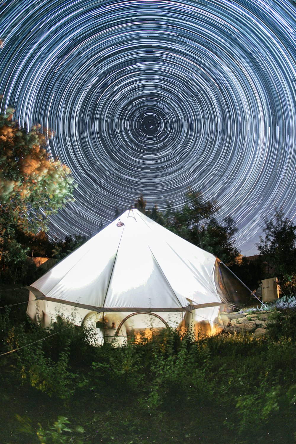 별이 가득한 하늘 아래 숲 한가운데에 앉아있는 커다란 흰색 텐트