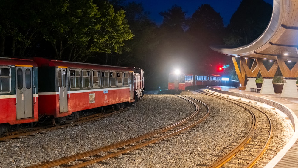a red train traveling past a train station at night