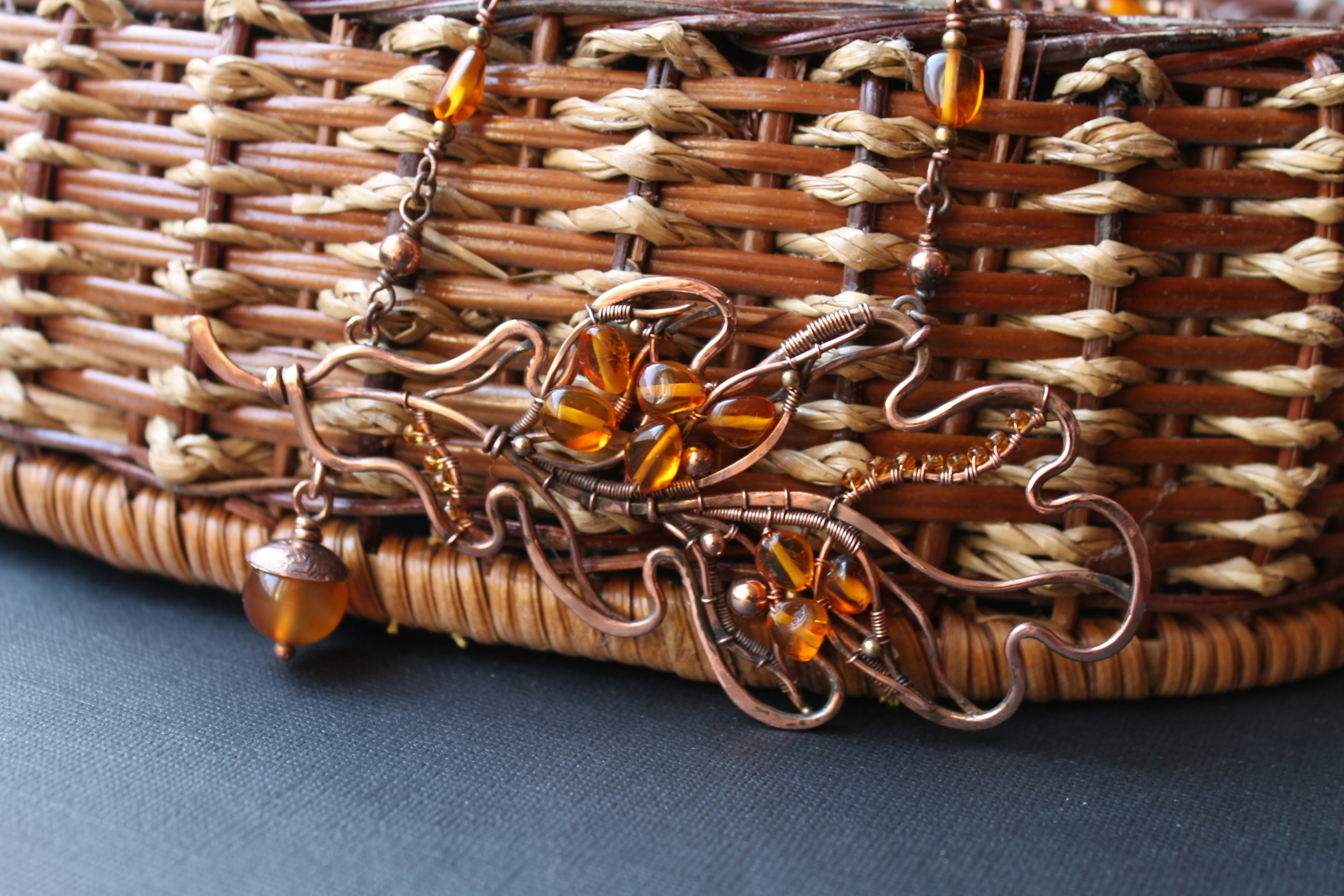 Collar artesanal de alambre de cobre con cuentas de ámbar sobre una cesta.