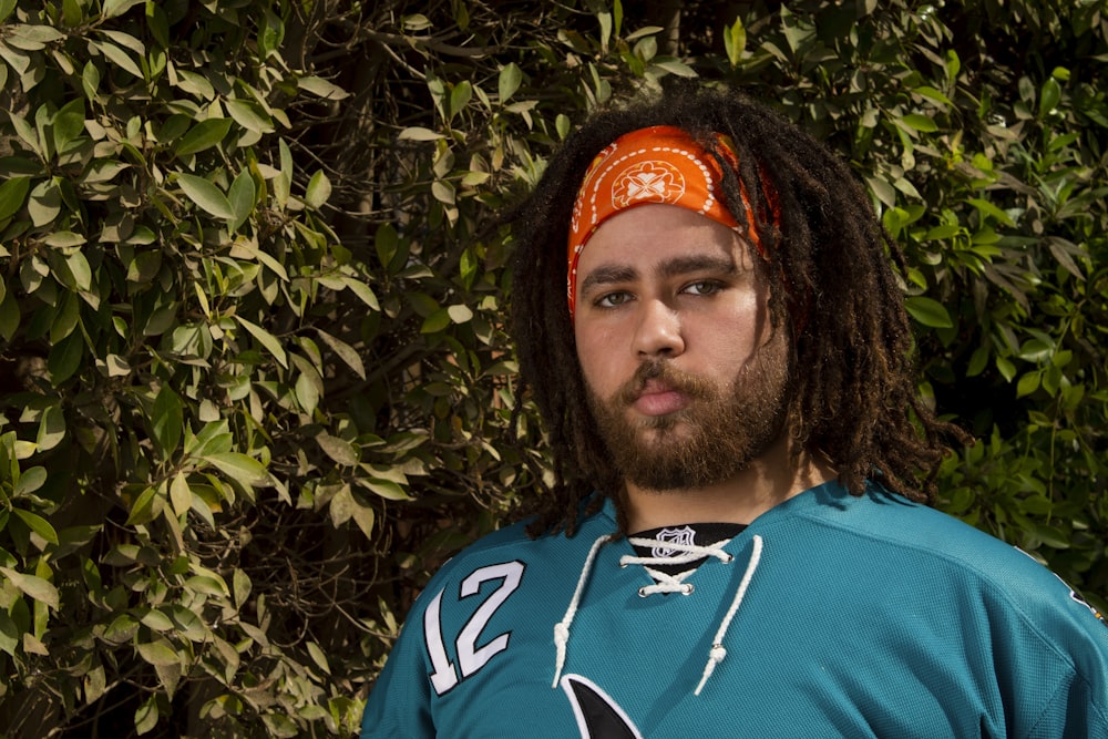 a man with dreadlocks standing in front of a bush