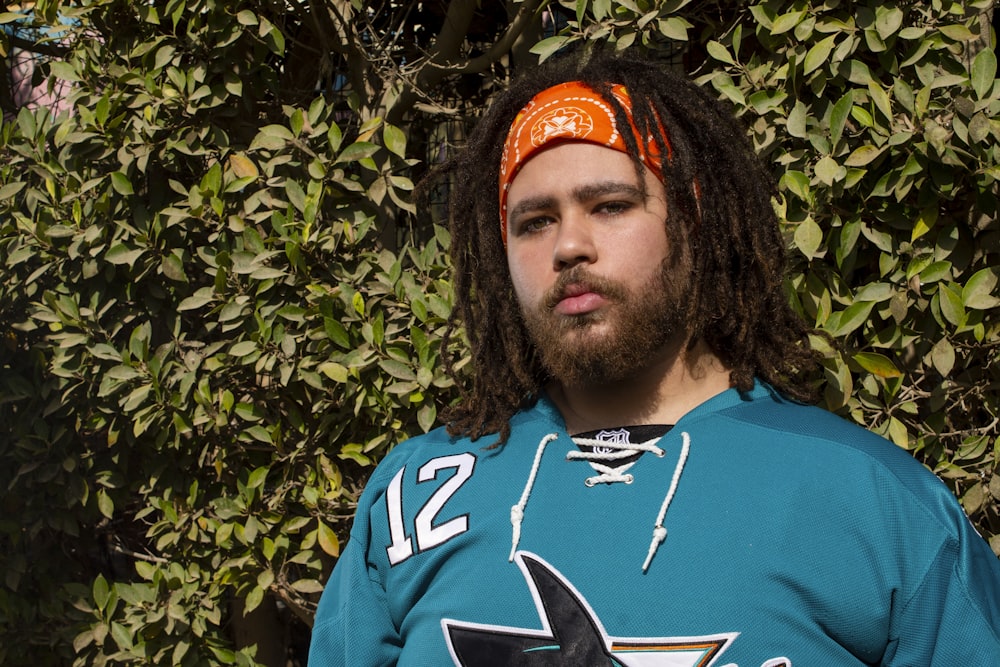 a man with dreadlocks standing in front of a bush