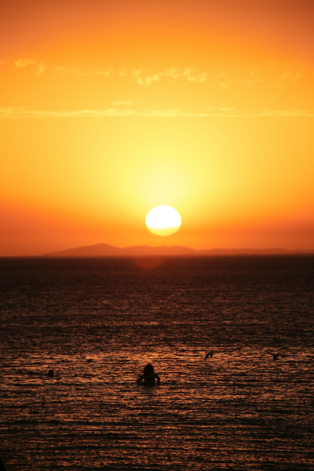 the sun is setting over the ocean with people swimming in the water