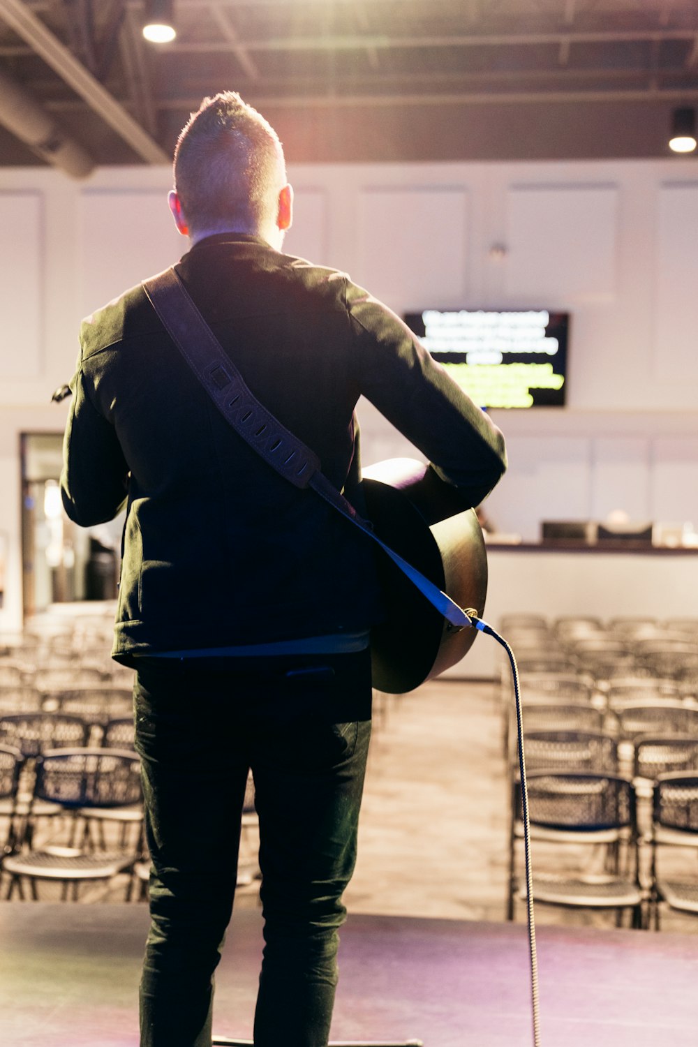 a man with a guitar stands in front of rows of chairs